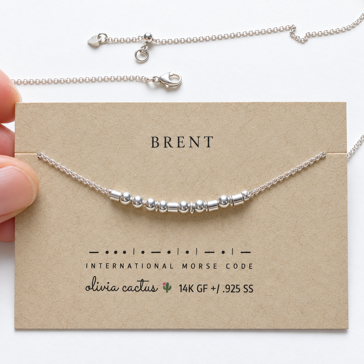 Hand holding the Extra Bold sterling silver Morse code necklace on its card, the name Brent spelled in Morse code beads